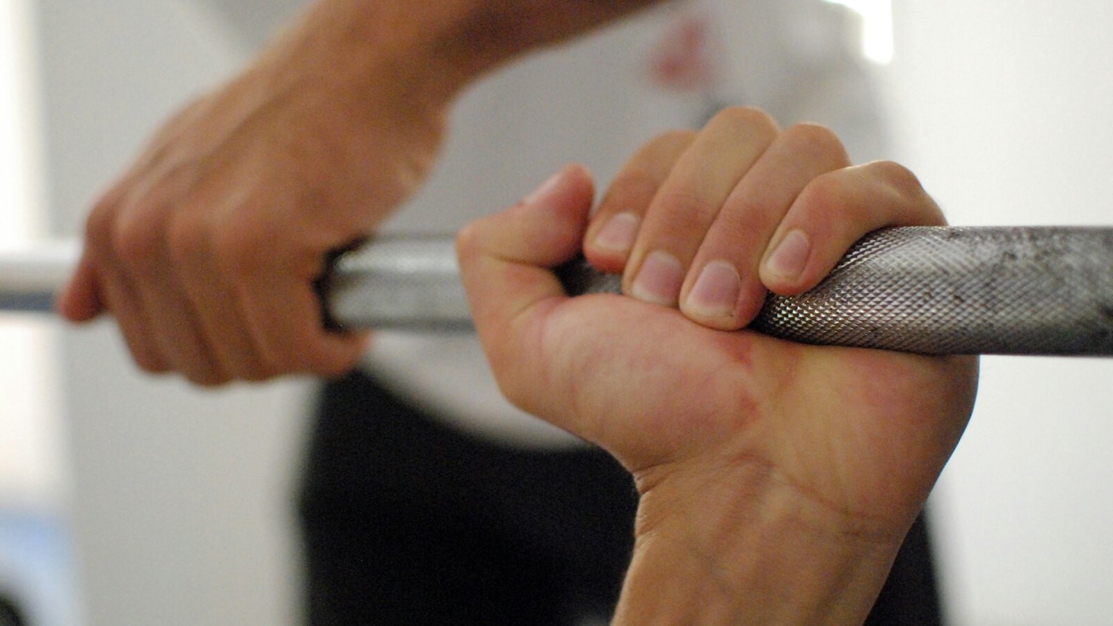 Chalked hands gripping a loaded barbell in low gym light